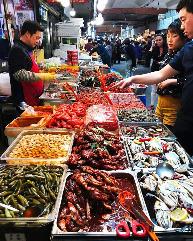 Vendor serving spicy seafood and banchan at a Korean traditional market
