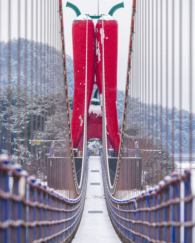 Suspension bridge with red gateposts crossing a snow-covered valley in Korea